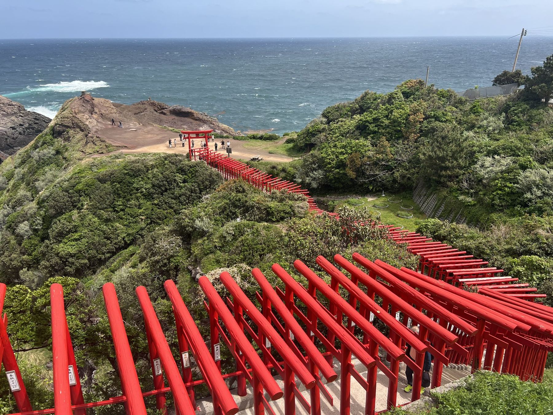 A line of vermilion torii gates descending a cliff to the sea